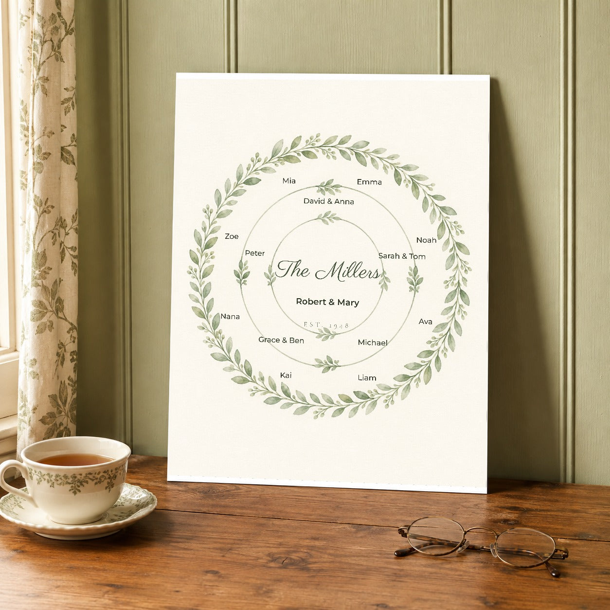 The unframed watercolor wreath print resting on a wooden table beside a teacup and reading glasses