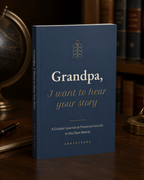 Grandpa, I Want to Hear Your Story guided journal standing on a wooden desk, navy softcover with gold lettering